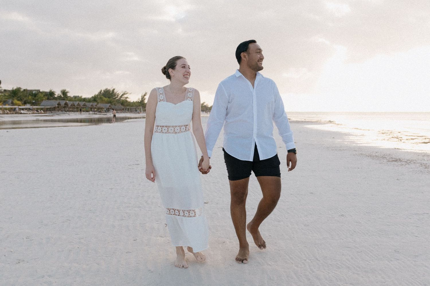 Joyful couple walking along a pristine white sandy beach at sunset.