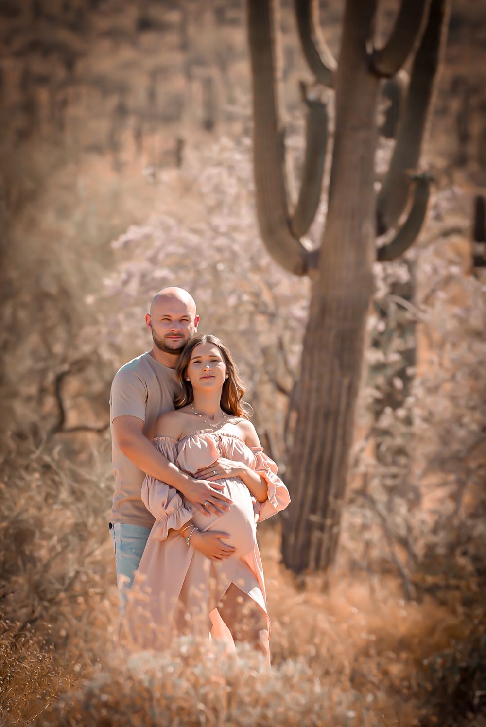 Expecting couple embracing in desert landscape with saguaro cactus during golden hour maternity shoot.