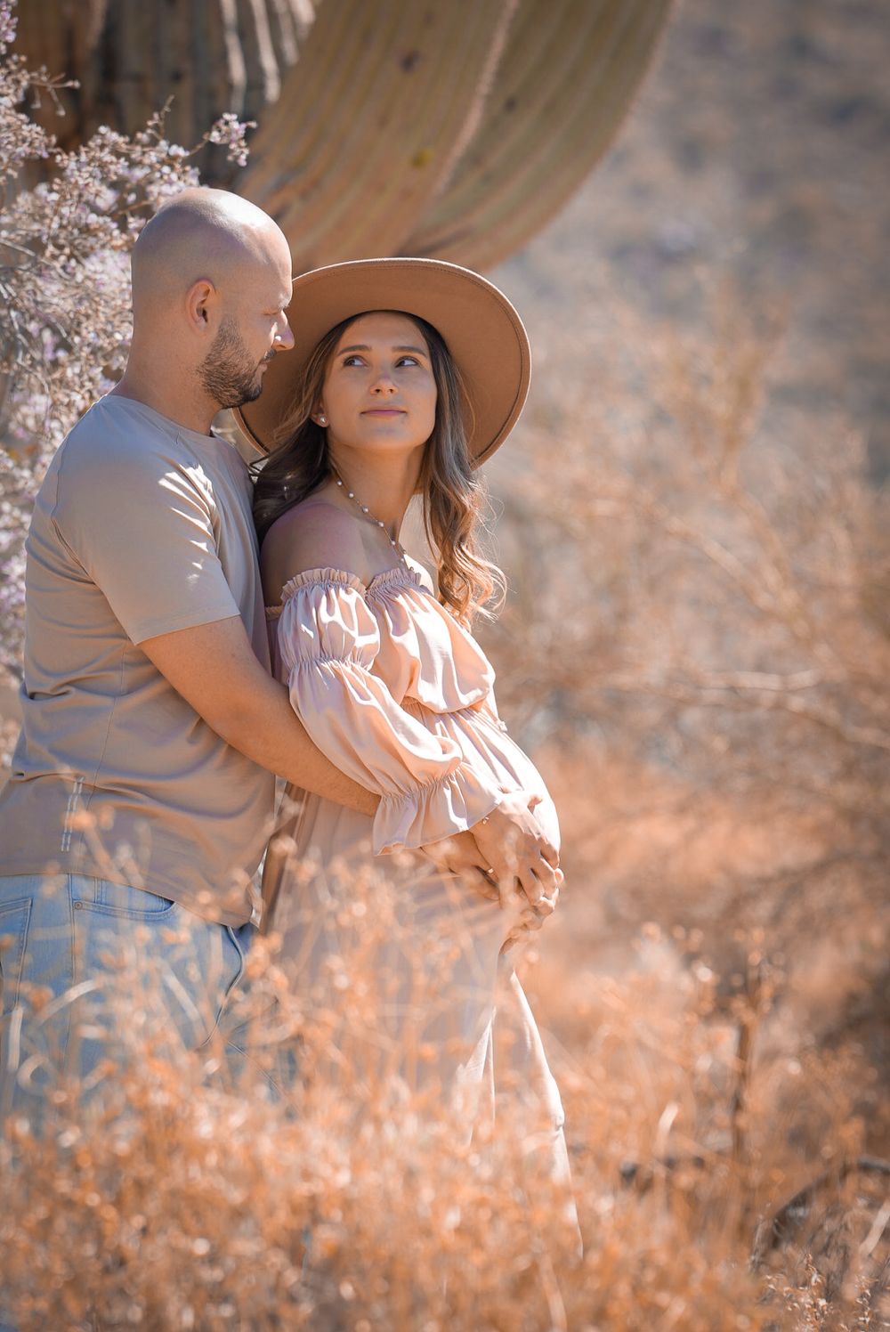Pregnant woman in pink dress and hat with partner in Arizona desert maternity photography.