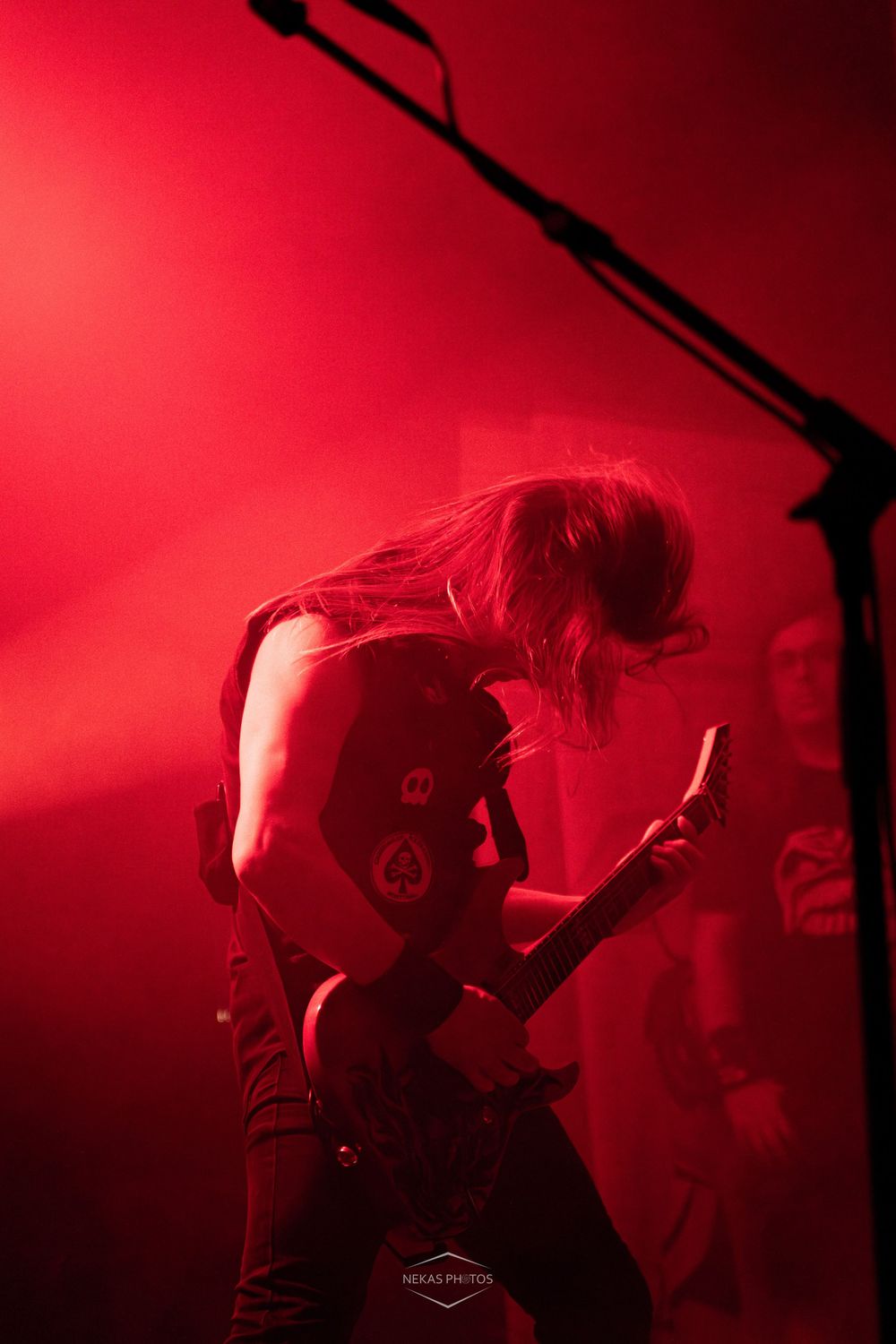 Metal guitarist performing on stage bathed in dramatic red light, hair flying as they shred electric guitar.
