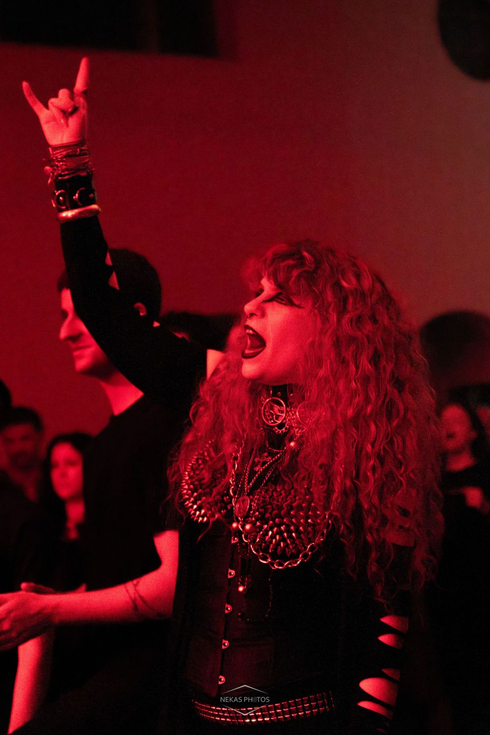 A woman with curly red hair throws the devil horns gesture while singing along at a metal concert.