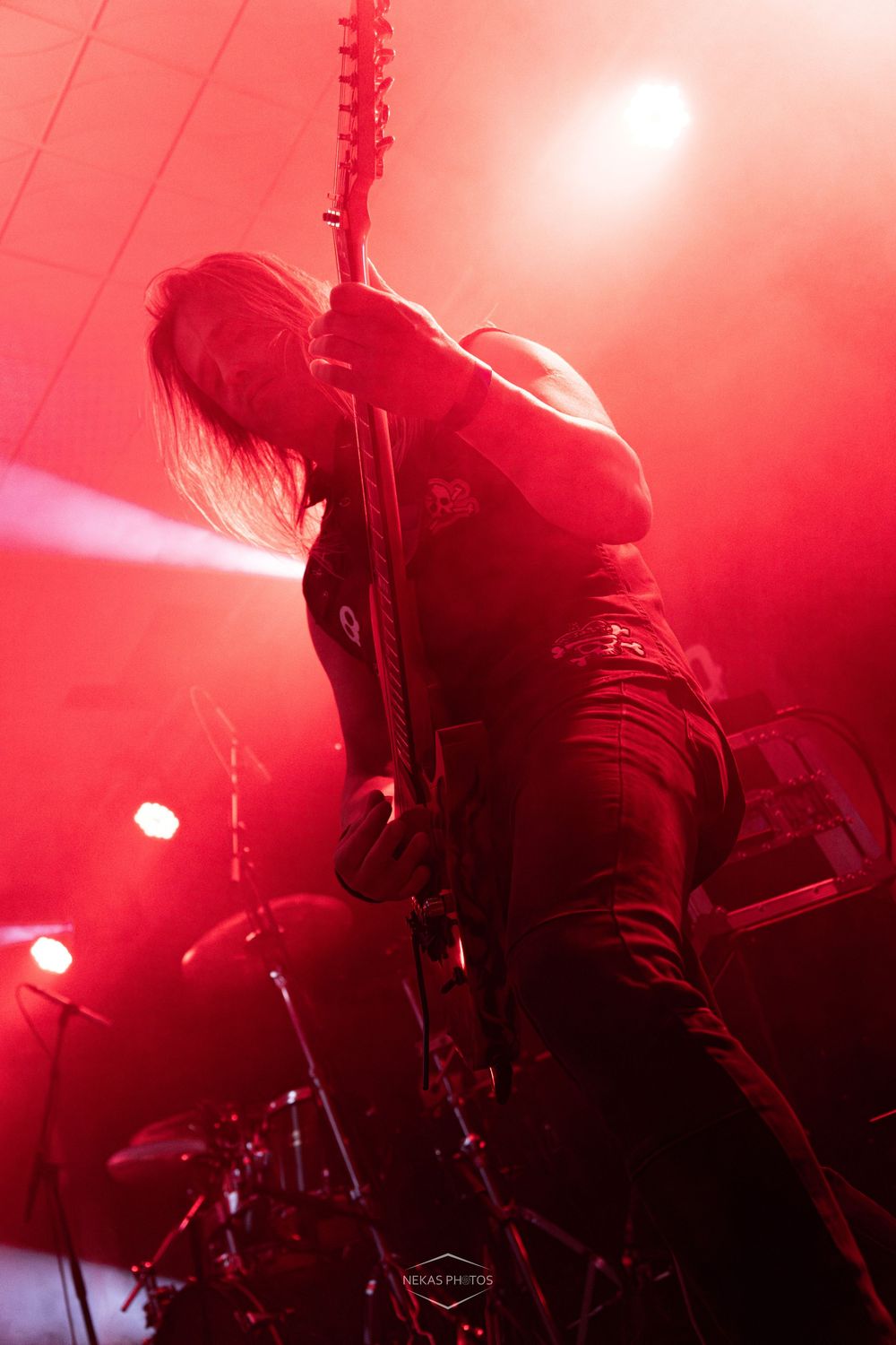 Guitarist performing on stage under dramatic red lighting at a heavy metal concert.