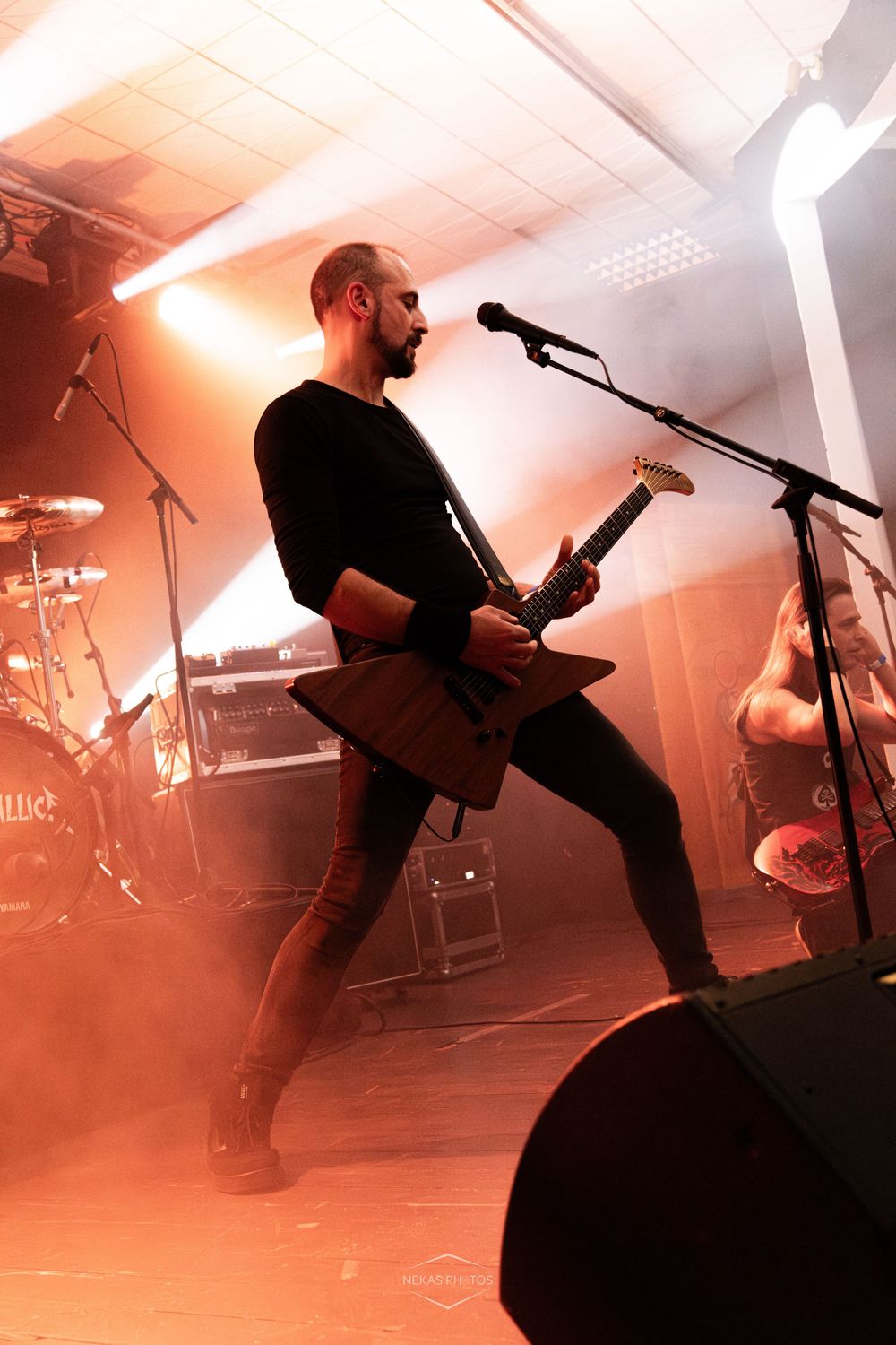 Male guitarist performing on stage with electric guitar, dramatic orange stage lighting and microphone stand at rock concert.