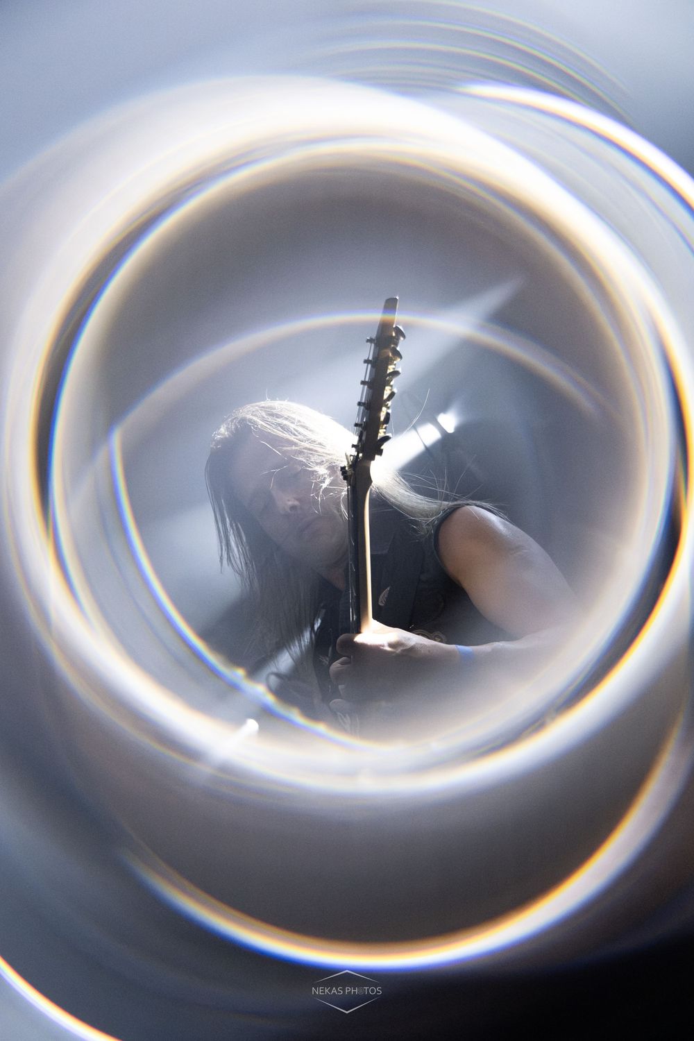 A rock guitarist with long hair holds an electric guitar, captured through a swirling lens effect creating circular light distortion.