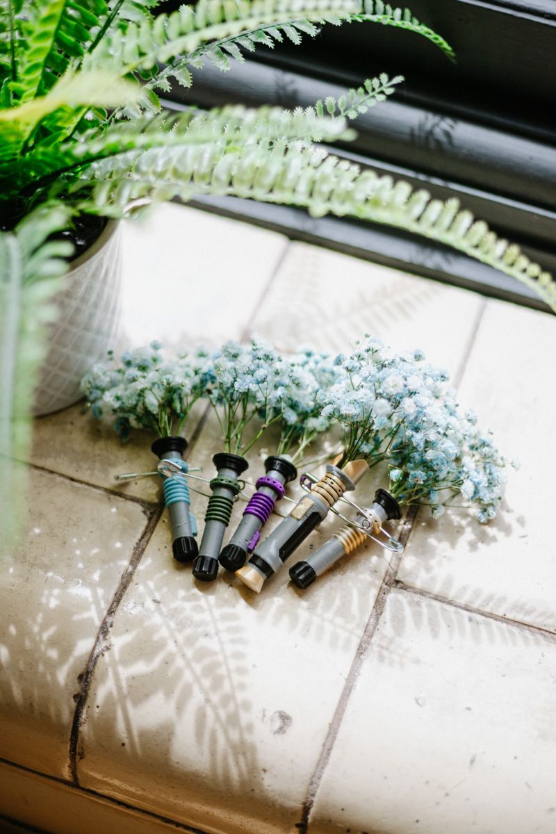 Lightsaber-handled bouquets of white baby's breath flowers arranged on a tiled surface near a fern plant.