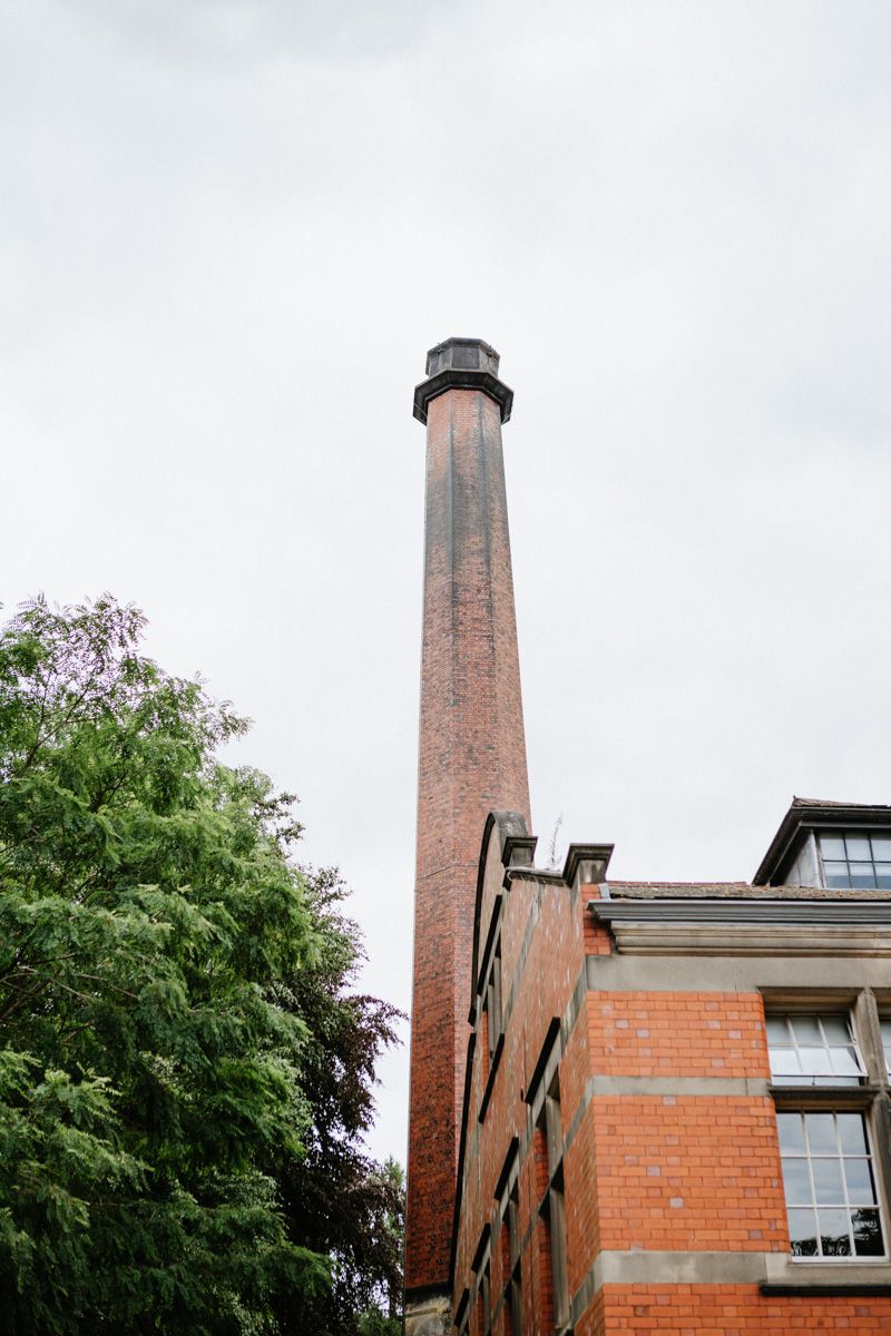 Tall red brick industrial chimney stack rising above a Victorian factory building against an overcast sky.