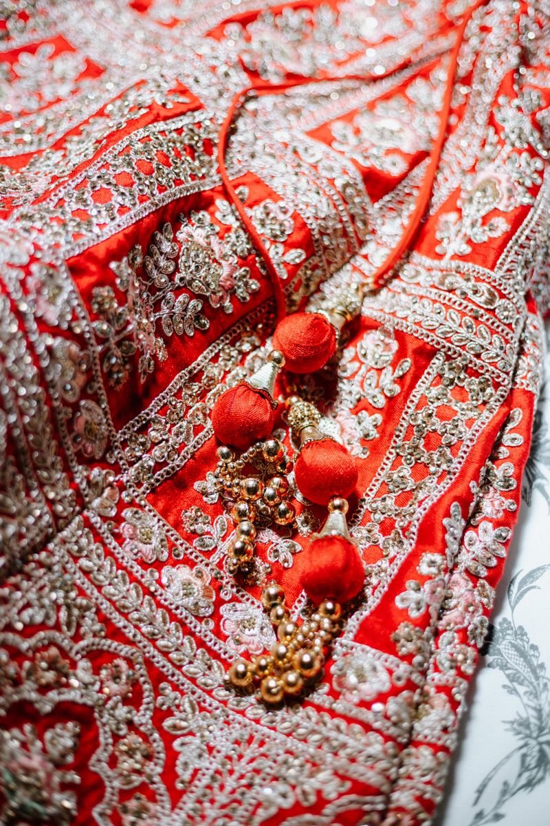 Intricate red and gold Indian bridal lehenga with silver embroidery, beadwork, and decorative tassels closeup.