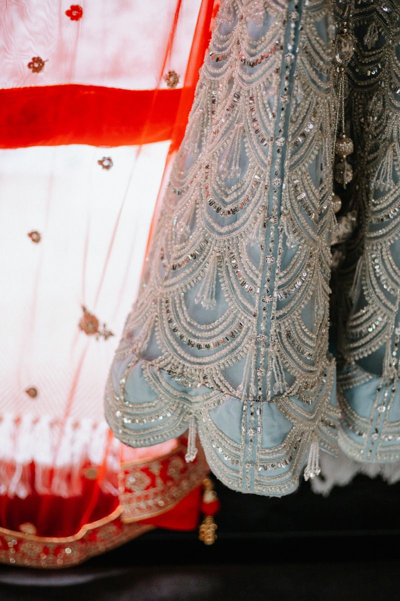 Intricate silver beaded Indian bridal lehenga beside a red dupatta with gold embroidery detailing.