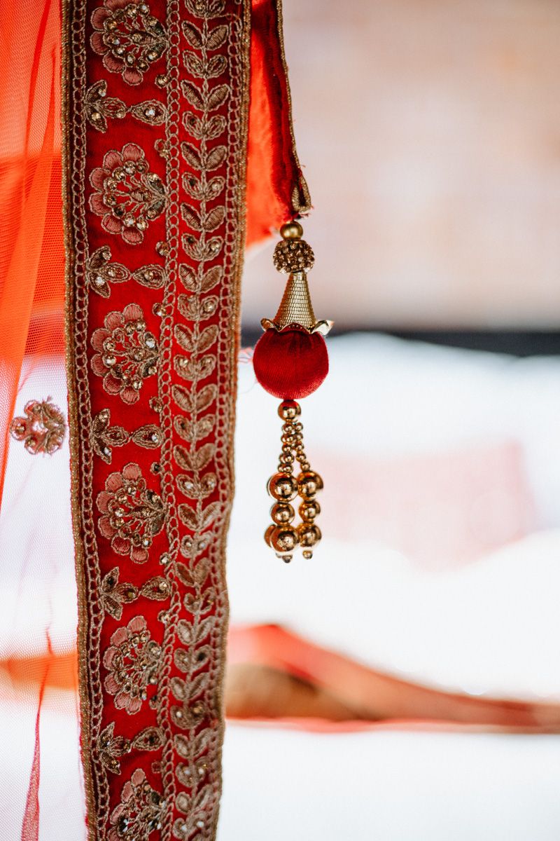 Red and gold embroidered Indian wedding mandap pillar with ornate tassel decoration and intricate floral patterns.