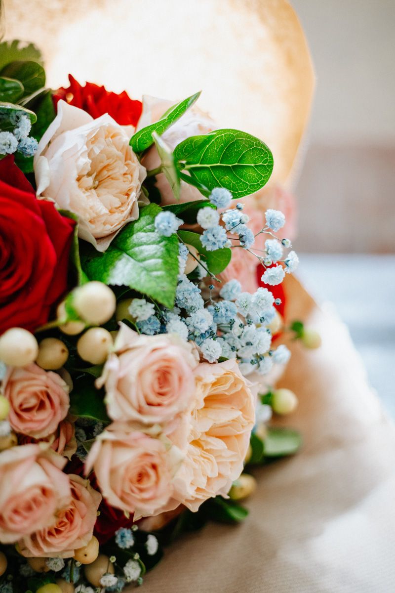 Elegant wedding bouquet featuring pink and red roses, white berries, and blue flowers with lush green leaves.