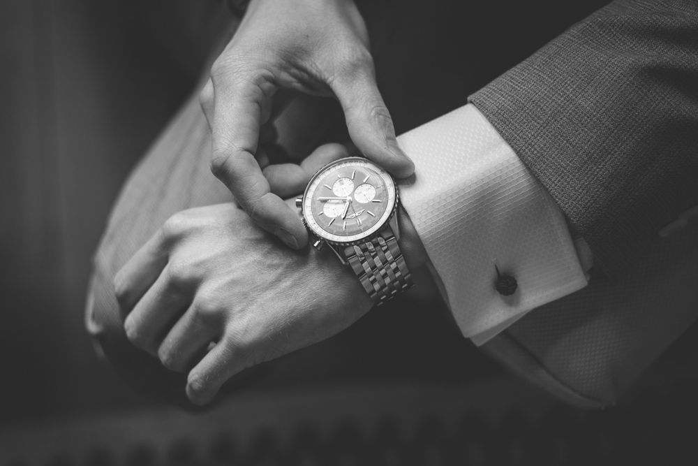 Black and white photo of a man in a suit adjusting a luxury chronograph watch on his wrist.