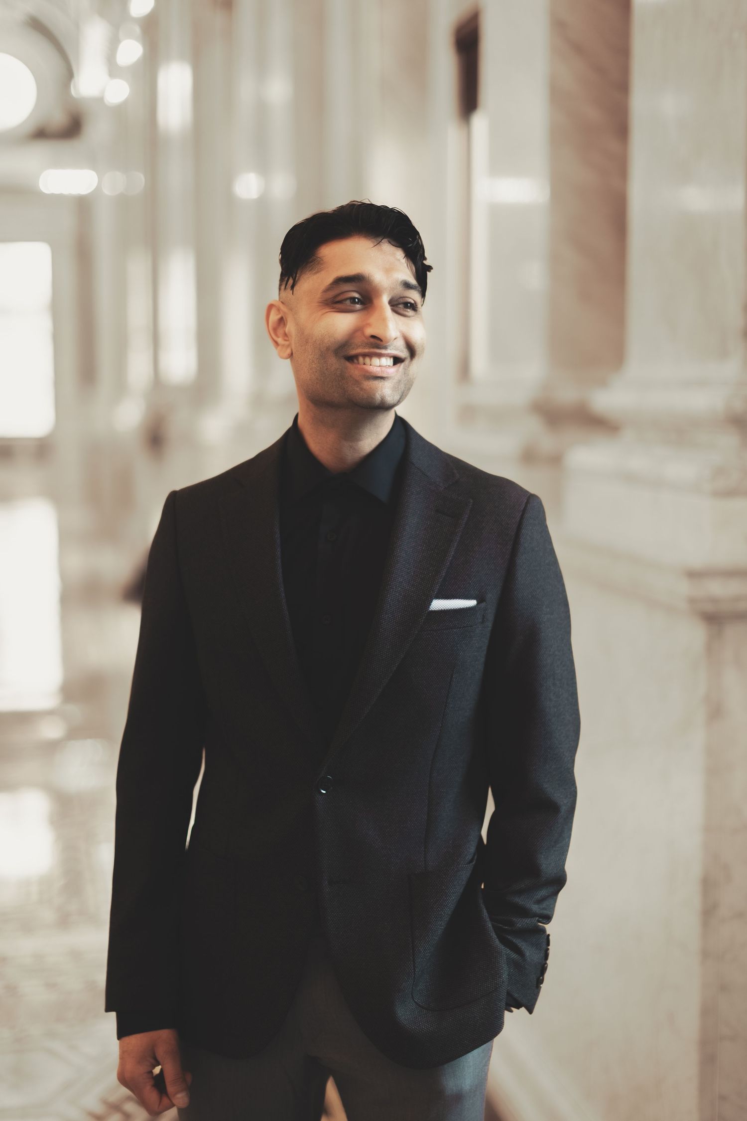 Smiling young man in black suit standing in elegant marble hallway during their library of congress photography session