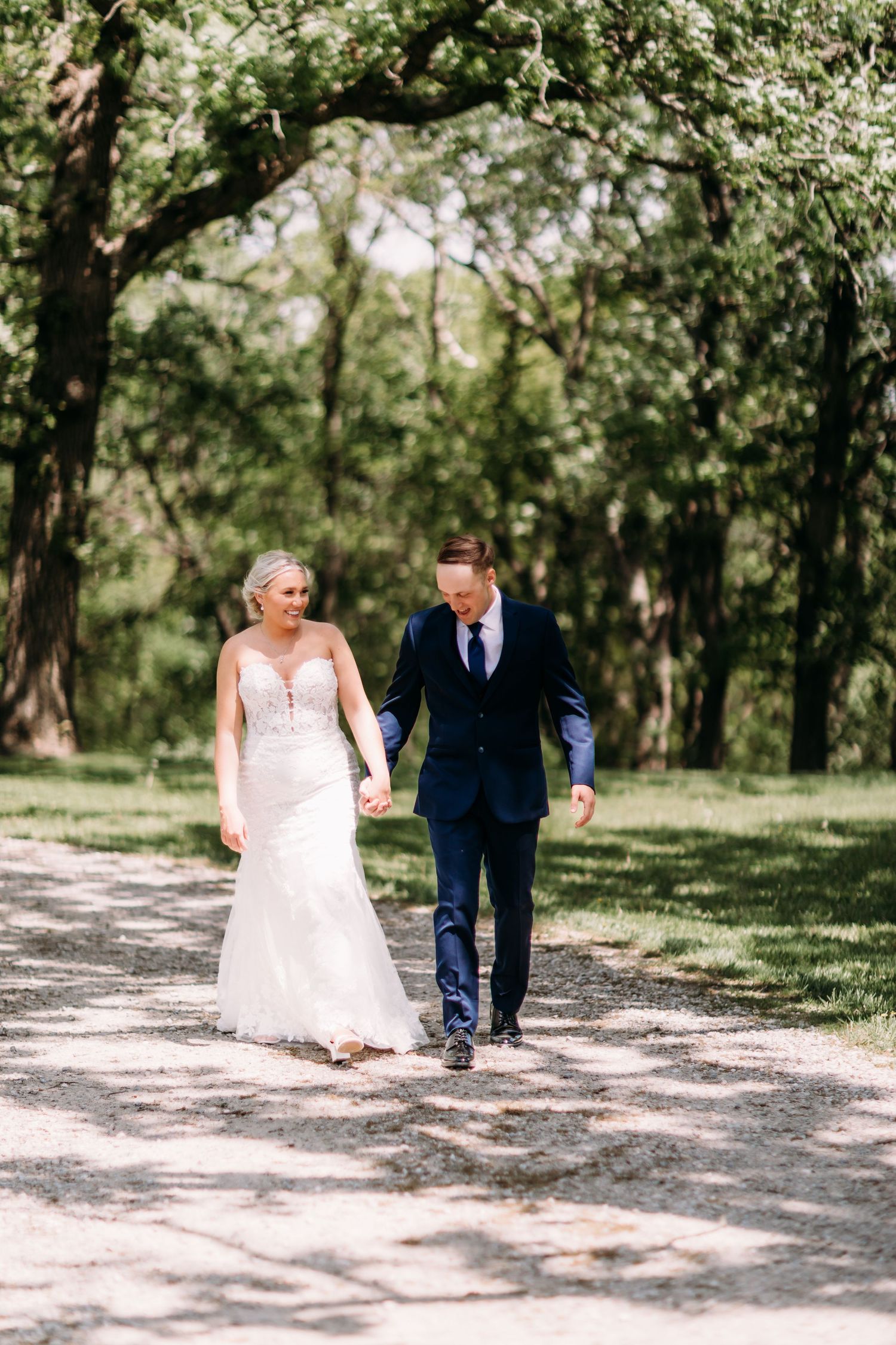 A bride and groom walk hand in hand along a tree-lined path on their wedding day.