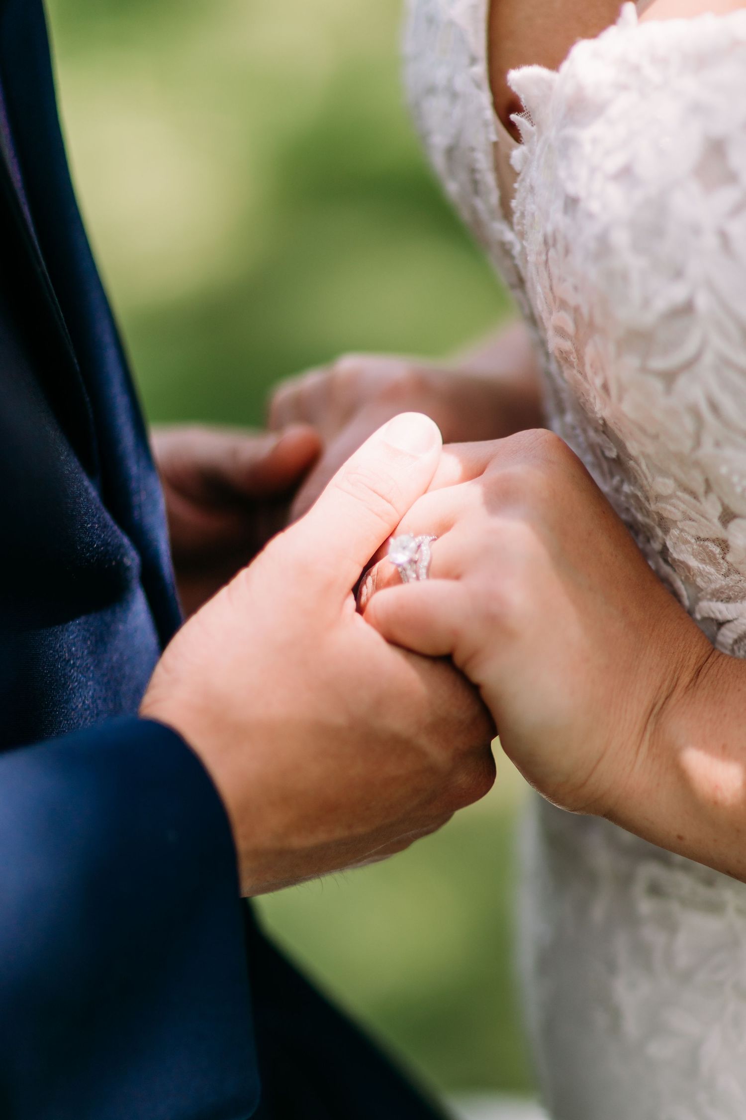 Bride and groom holding hands during wedding ceremony, showcasing a sparkling diamond engagement ring.