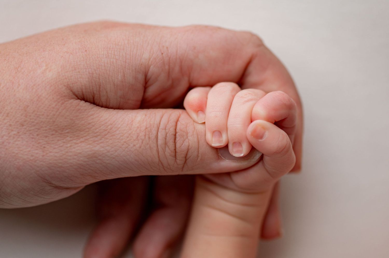 Sleeping newborn baby in olive green romper with fists raised, posed on matching green backdrop.