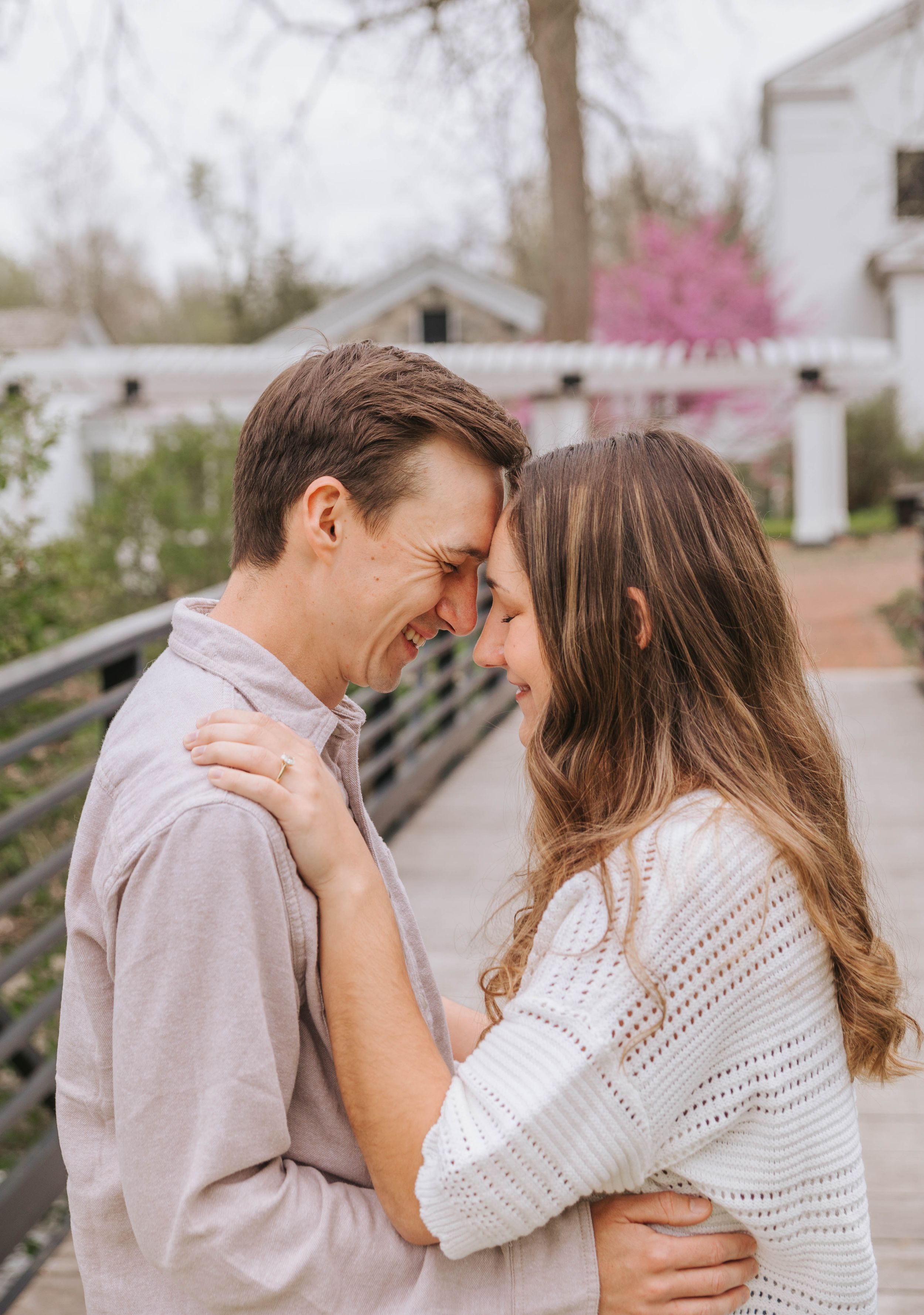 Couple sharing a romantic forehead touch outdoors on a bridge, surrounded by spring blooms.