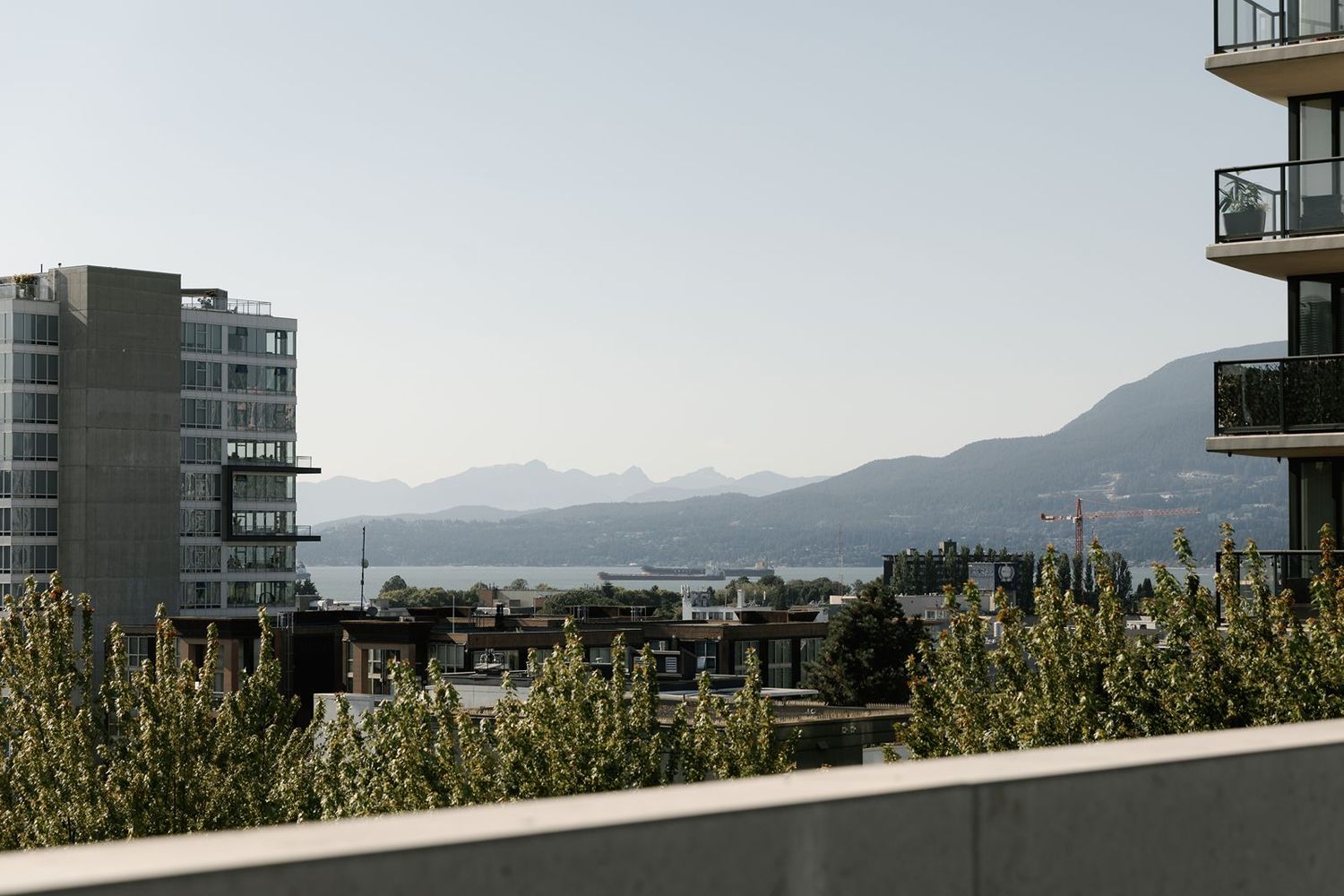 Panoramic rooftop view of Vancouver cityscape with mountains and ocean in the background on a clear day.