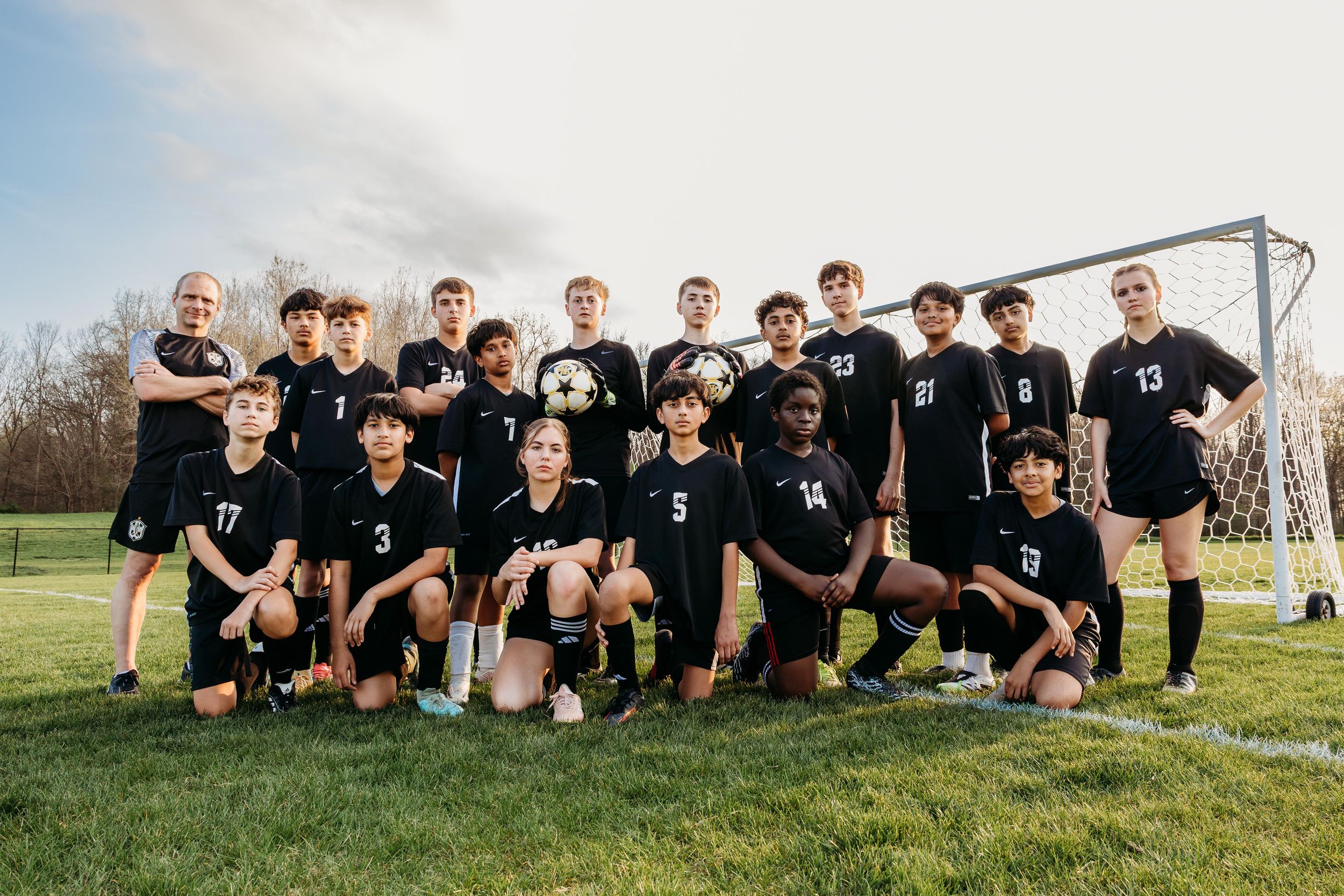 Boys soccer team in black uniforms posing together on grass field in front of goal post.