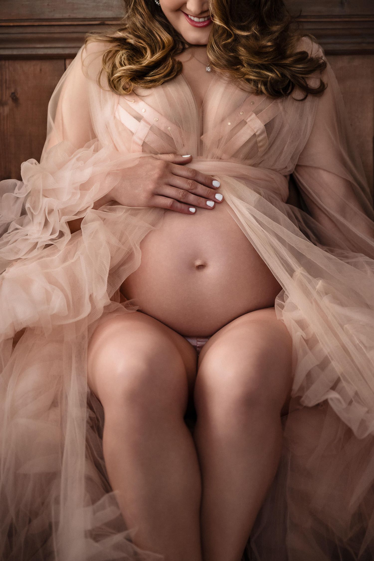 Maternity boudoir photo with flowing blush tulle fabric draping over a pregnant figure. pregnancy boudoir photoshoot