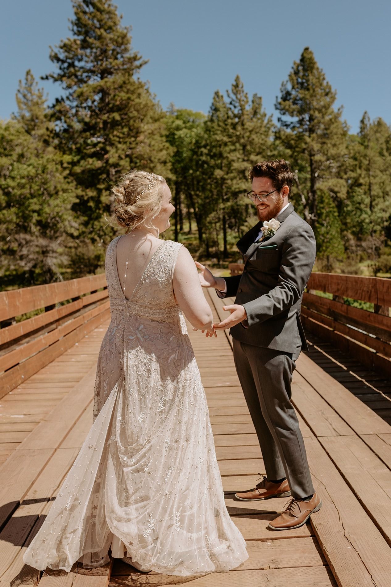 Bride and groom hold hands on a wooden bridge surrounded by pine trees during an outdoor wedding ceremony at Lake Cuyamaca, Julian.