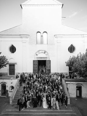 Large wedding group portrait on church steps in black and white, featuring bride and groom at center.
