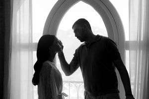 Black and white silhouette of a couple standing by an arched window, sharing an intimate romantic moment.