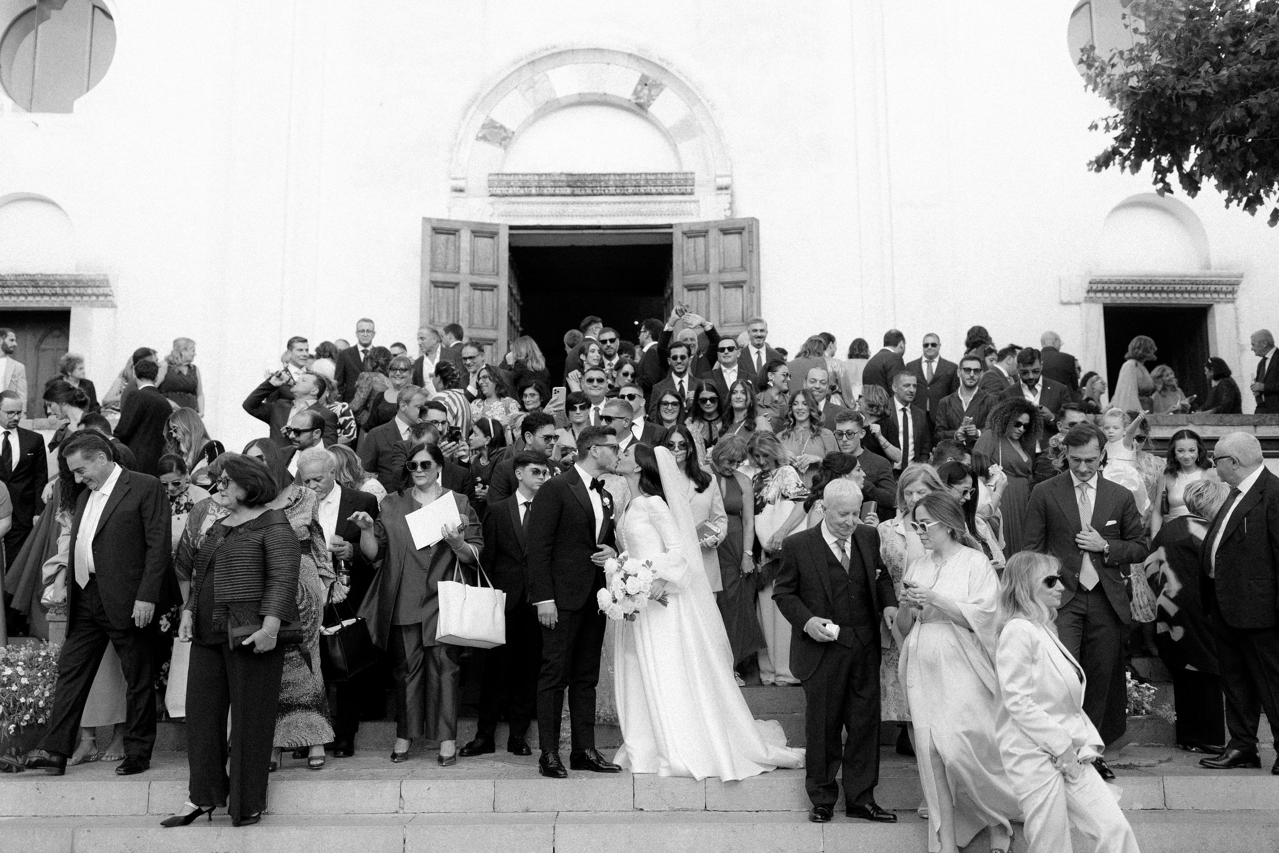 Black and white photo of a wedding party and guests gathered on church steps after a ceremony.
