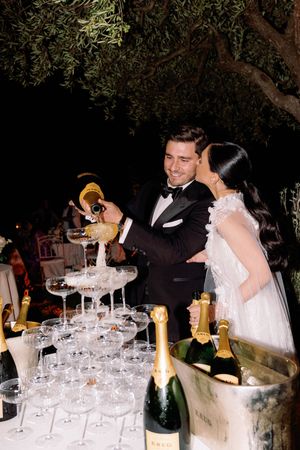 Bride and groom pouring champagne tower at elegant wedding reception outdoors at night with Moet bottles.