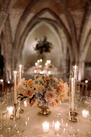 Elegant wedding table with blush floral centerpiece, tall candles, and glassware in a candlelit stone arch venue.