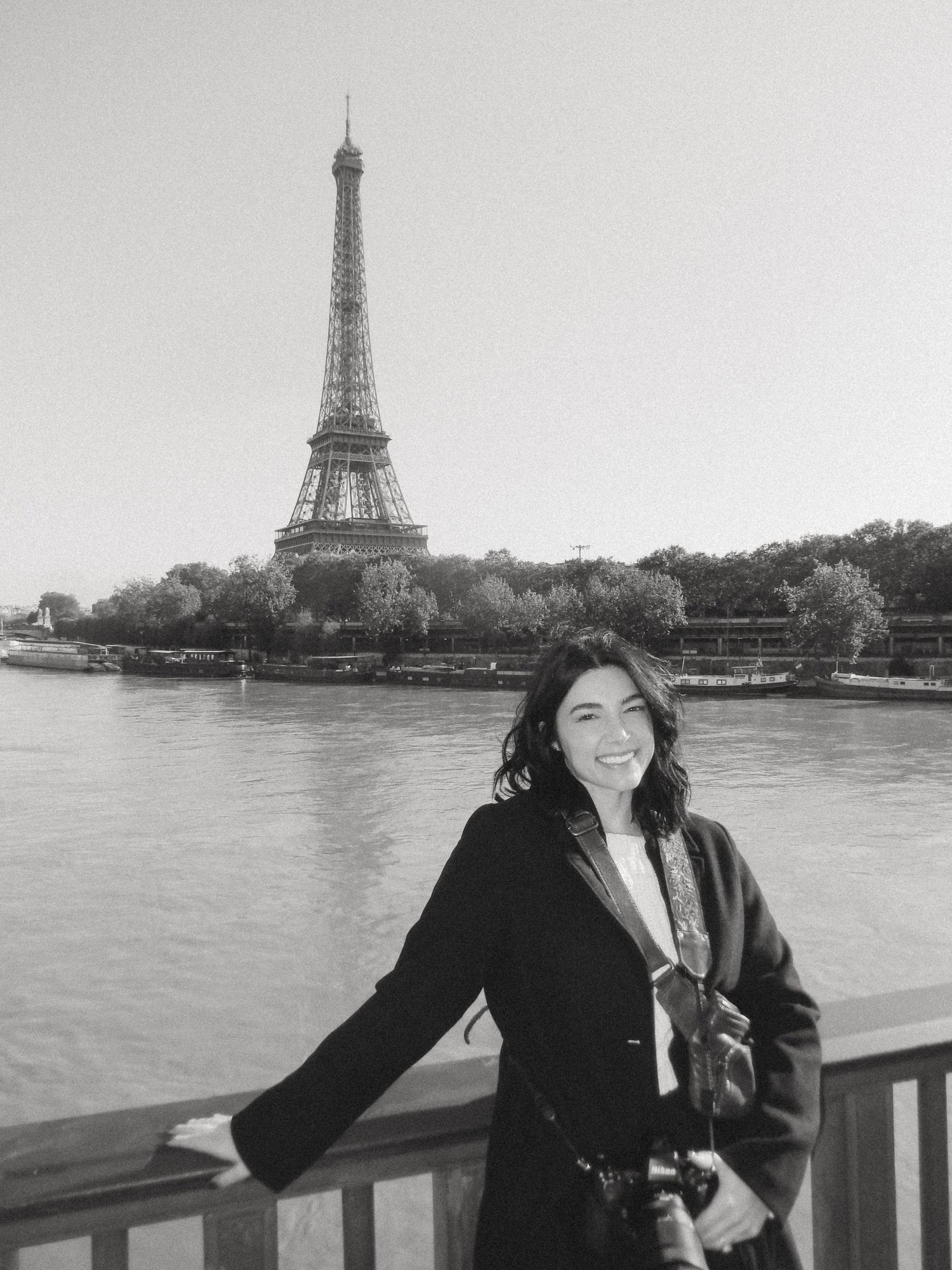 Woman smiling in front of the Eiffel Tower and Seine River in Paris, black and white photo.