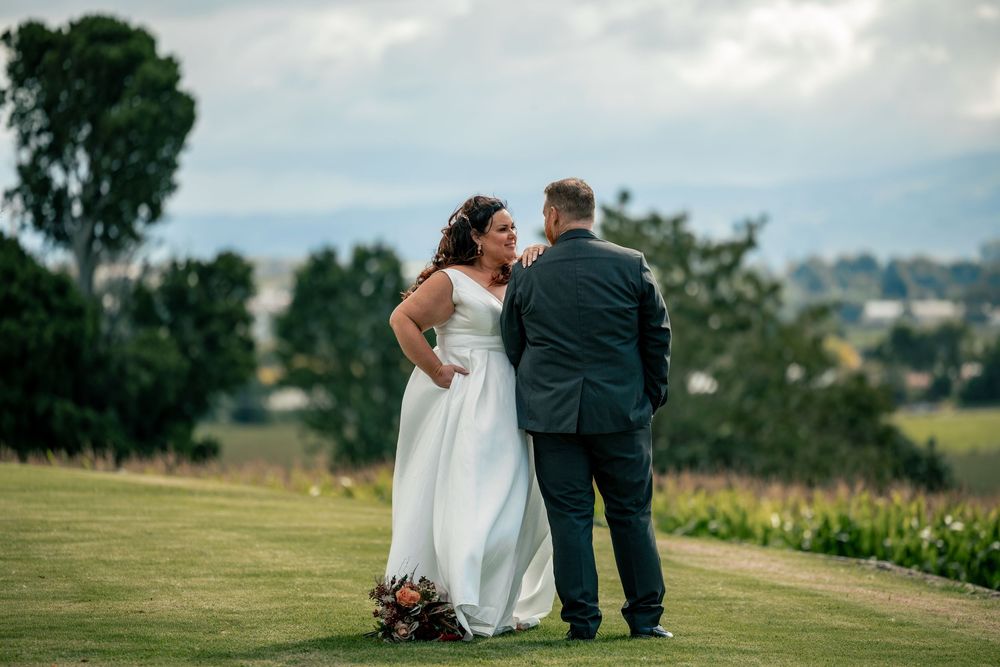 Bride and groom share a tender moment on a lush green lawn with scenic countryside views behind them.