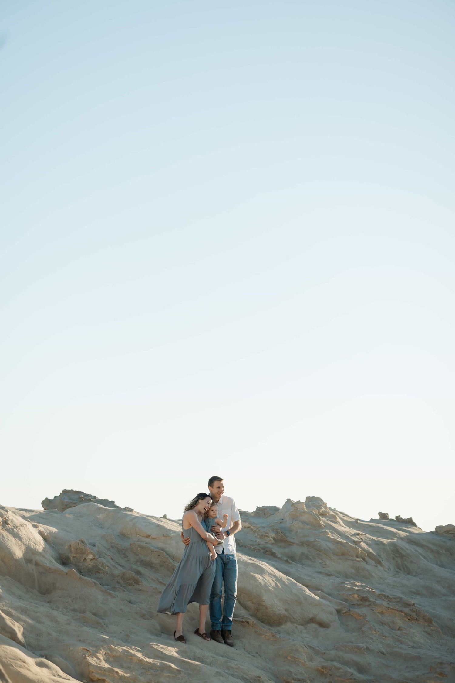 Couple embracing on rocky terrain against a clear blue sky at golden hour.