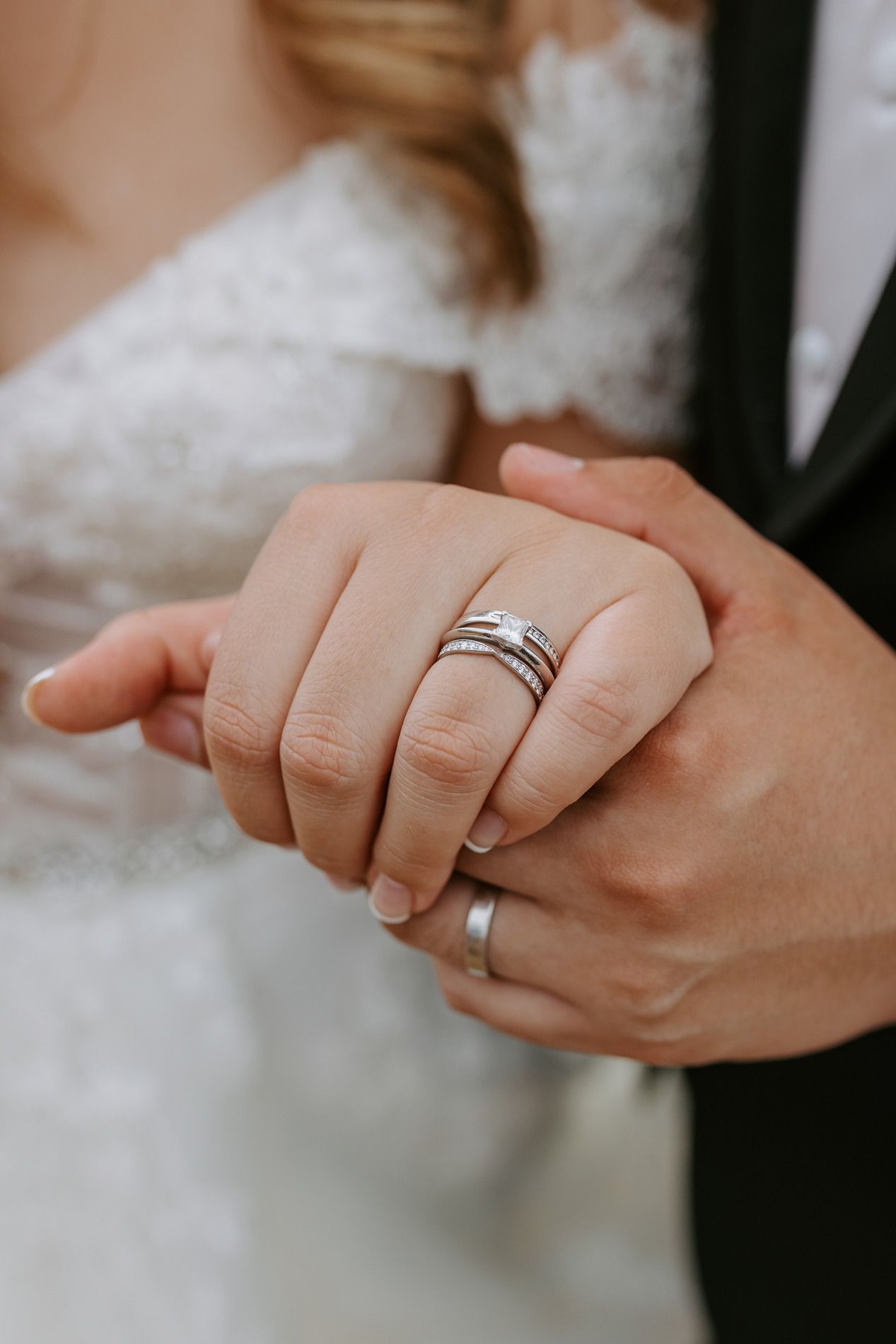 Bride and groom holding hands showing silver wedding bands and diamond engagement ring on their wedding day.