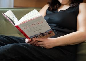 Woman in black dress reading Suzuki book by Eri Hotta while relaxing on a green couch.