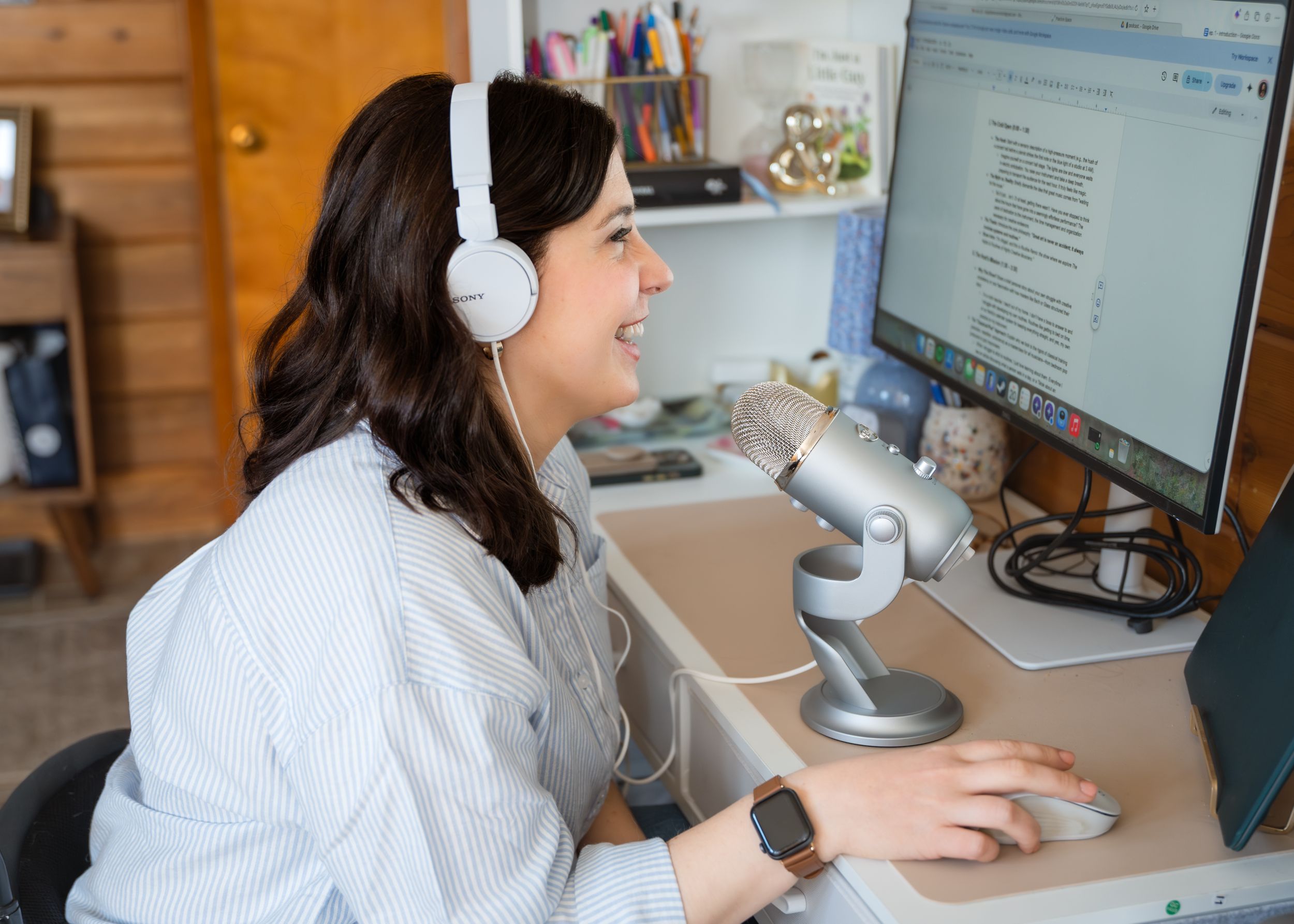 Woman with headphones speaks into microphone at desktop computer workstation.