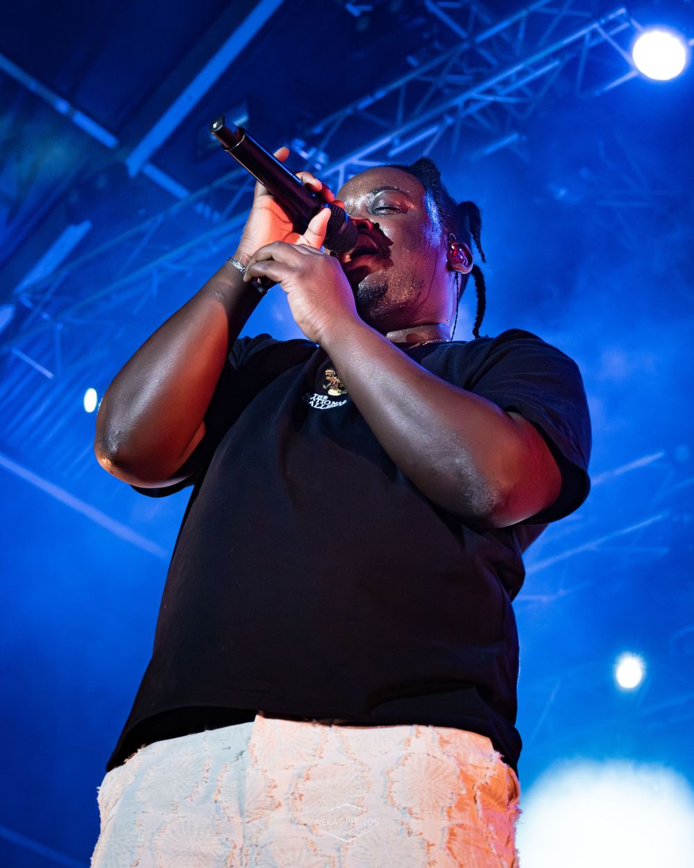 Male performer singing into microphone on stage with blue concert lighting backdrop.