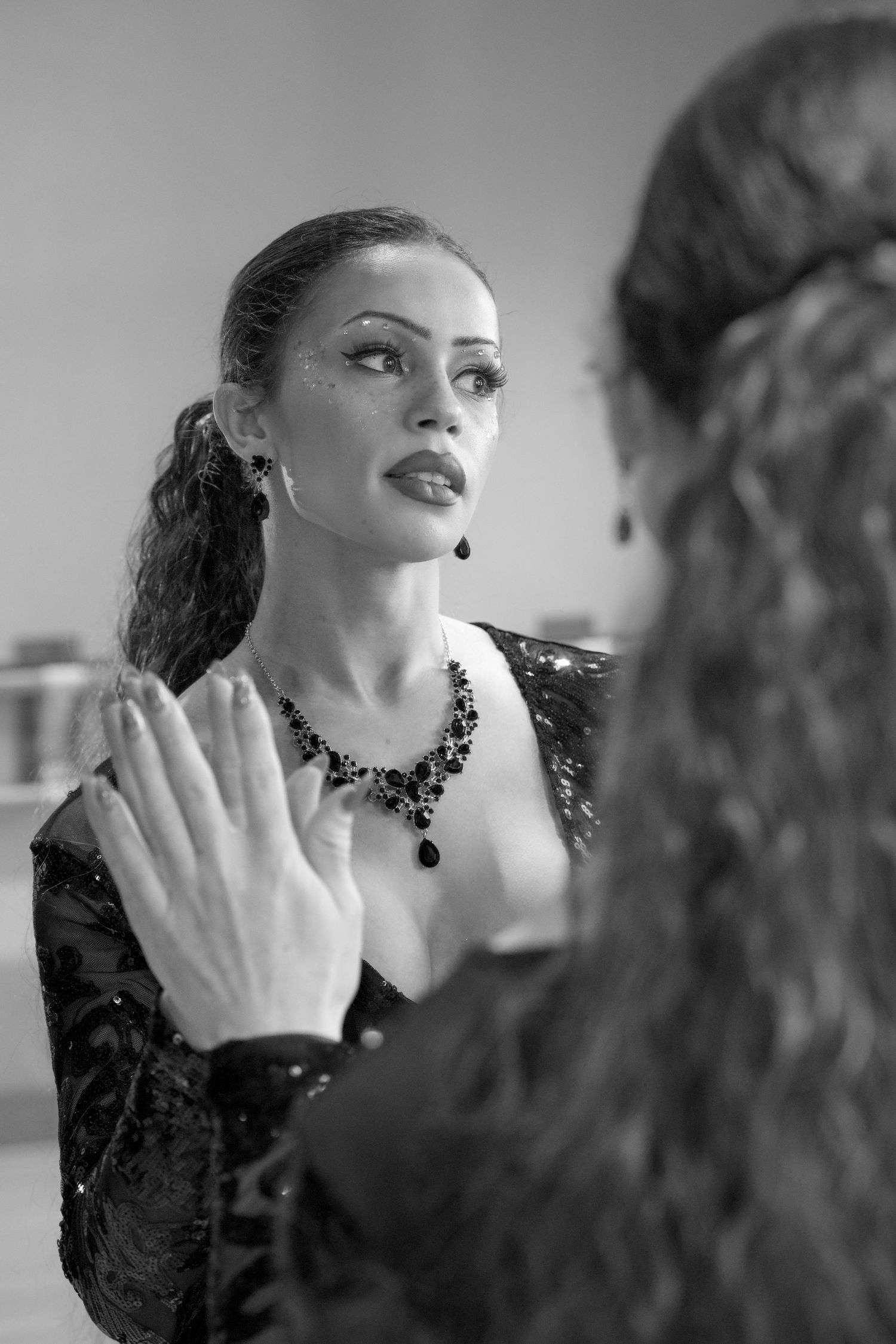 Black and white photo of an elegant woman in sequined dress with jeweled necklace, looking in mirror.