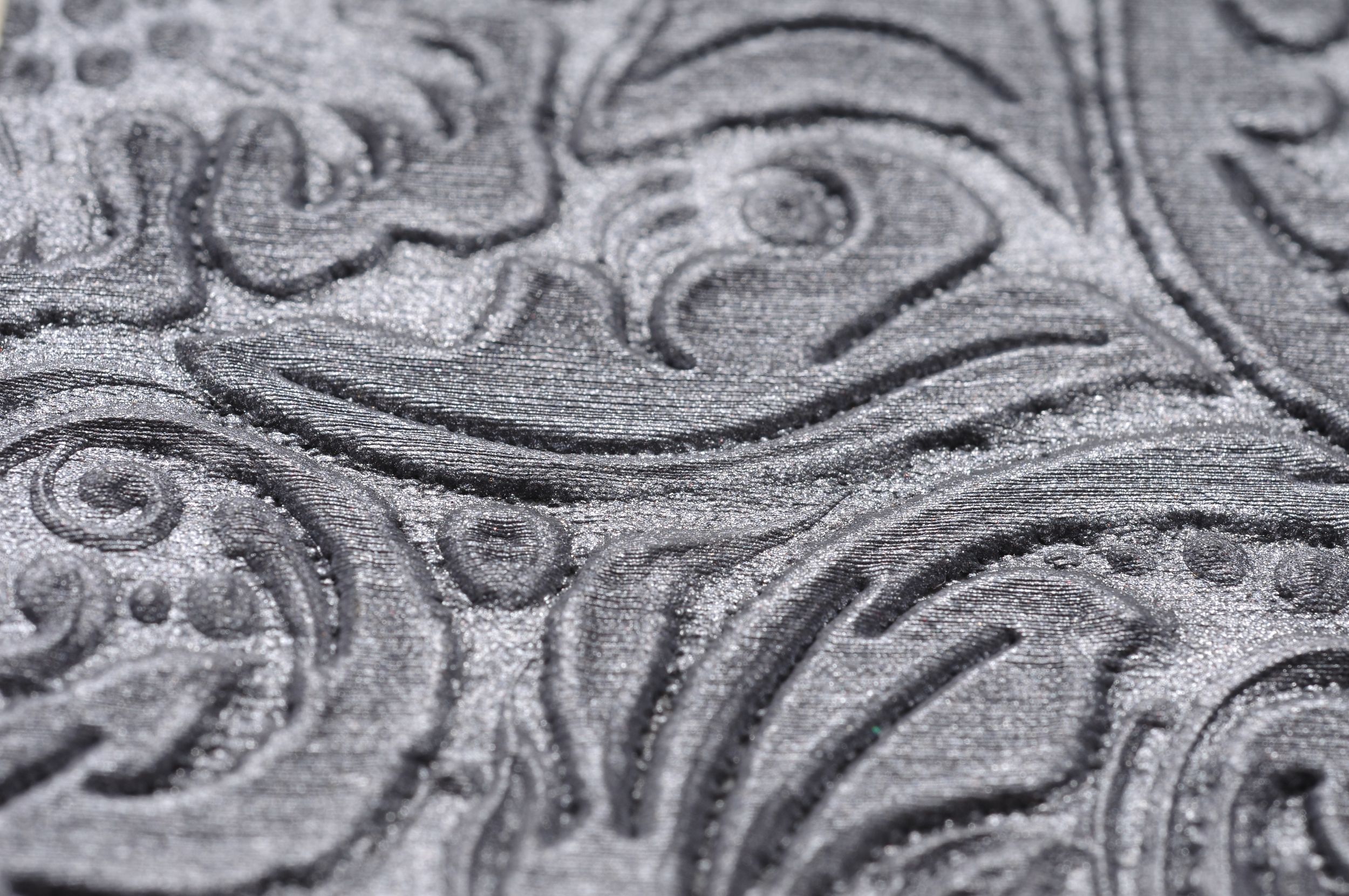Extreme close-up macro photography of an embossed silver metal surface showing detailed swirling floral patterns.