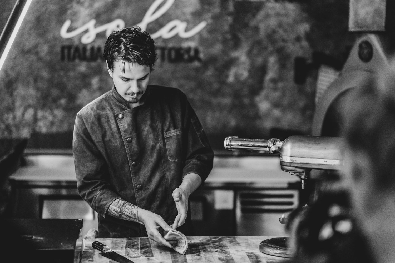 Chef with tattoos prepares fresh pasta at Isola Italian Trattoria in a black and white culinary photo.