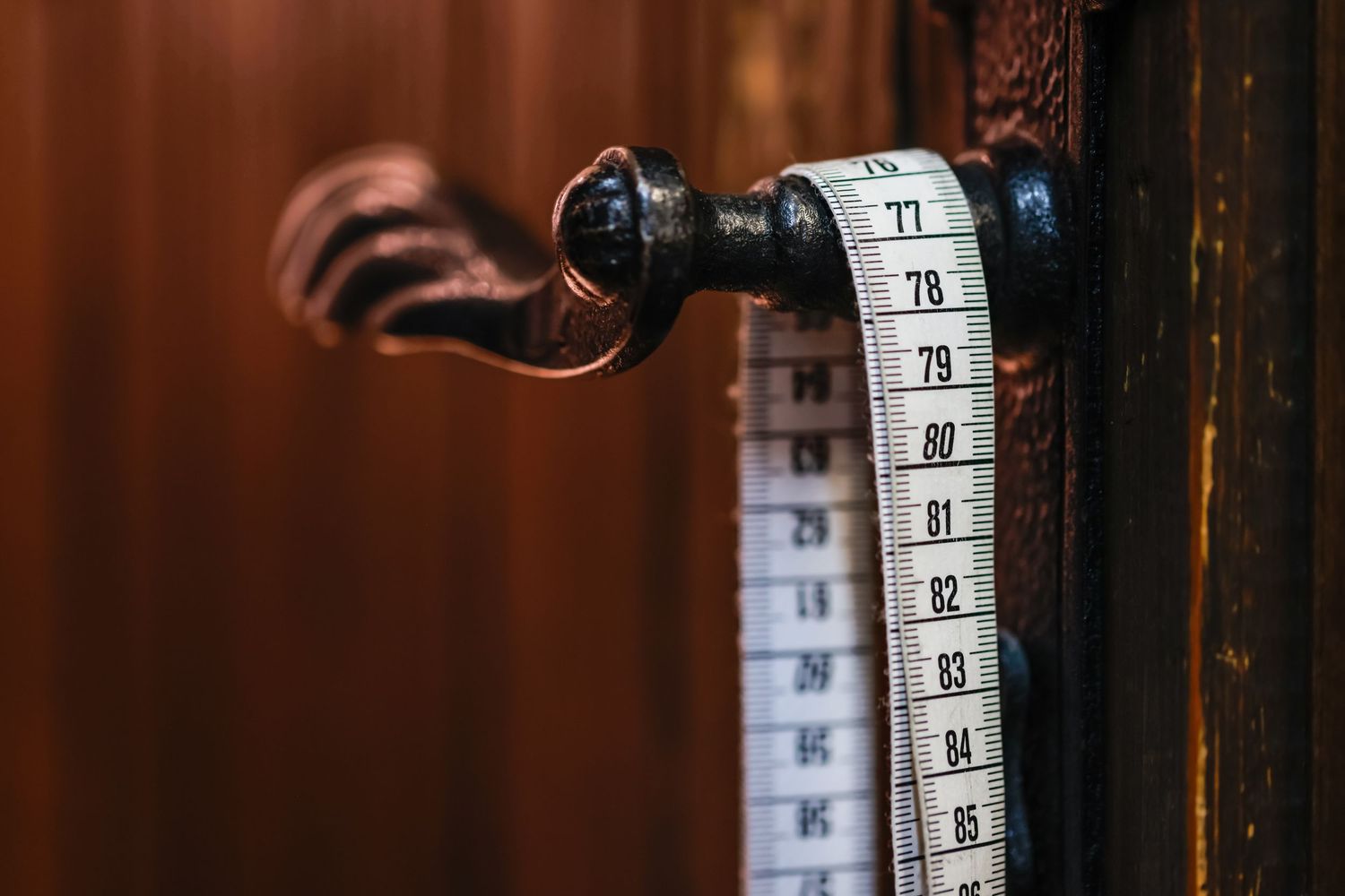 A vintage door handle with a measuring tape draped over it, showing measurements from 77 to 95.