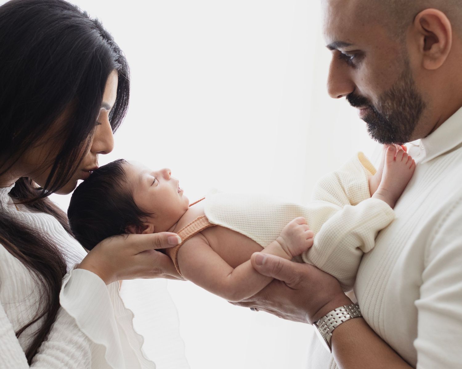 New parents lovingly gaze at their newborn baby, cradling the infant gently in a bright, softly lit room. Elizabeth Lang Surrey