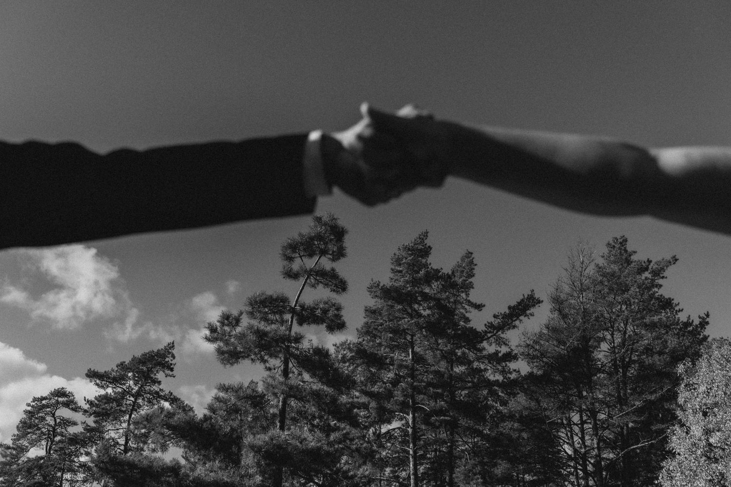 Mustavalkoinen yksityiskohtakuva käsistä, jotka koskettavat toisiaan taivasta vasten.