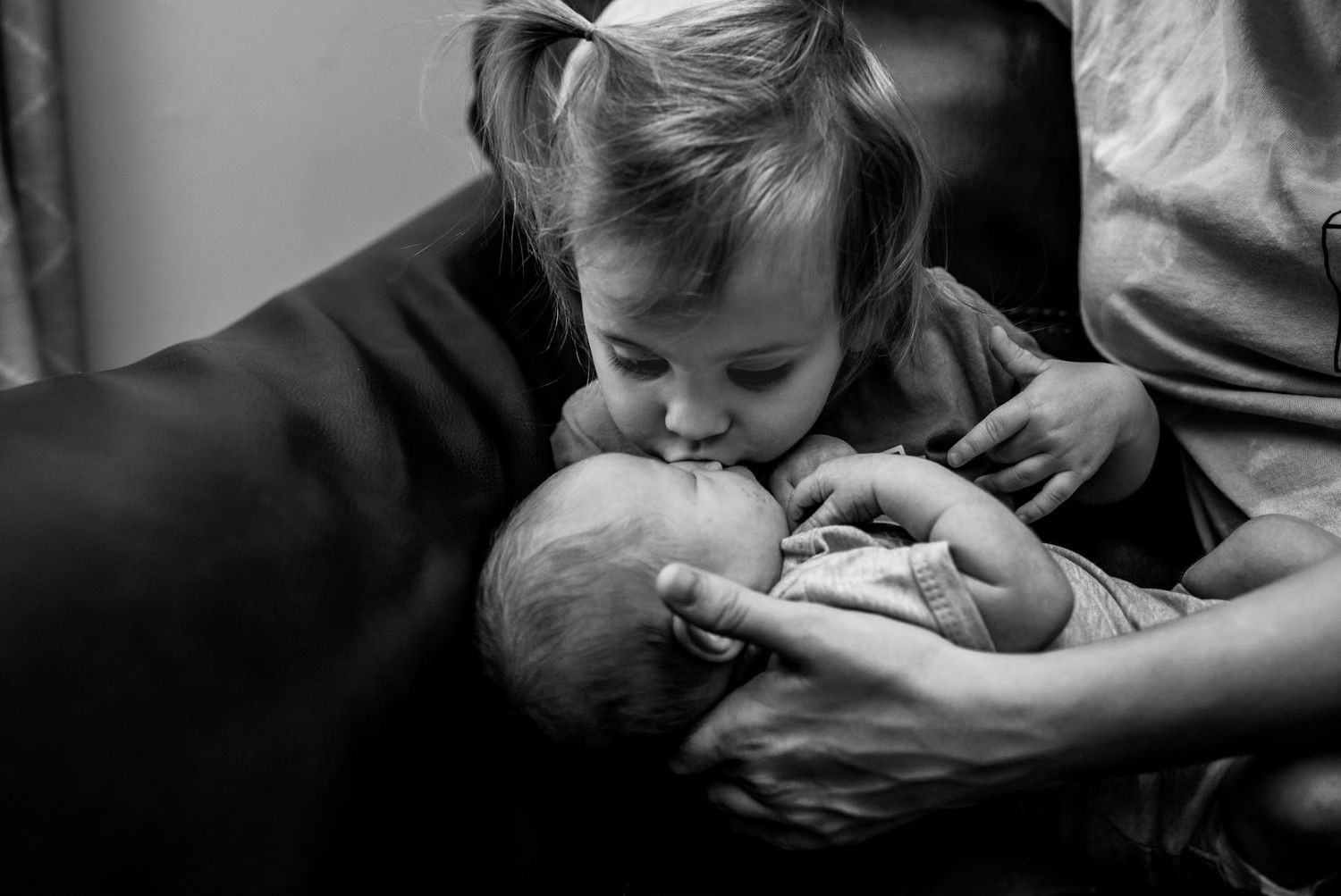 Black and white image of tender sibling moment with newborn baby.