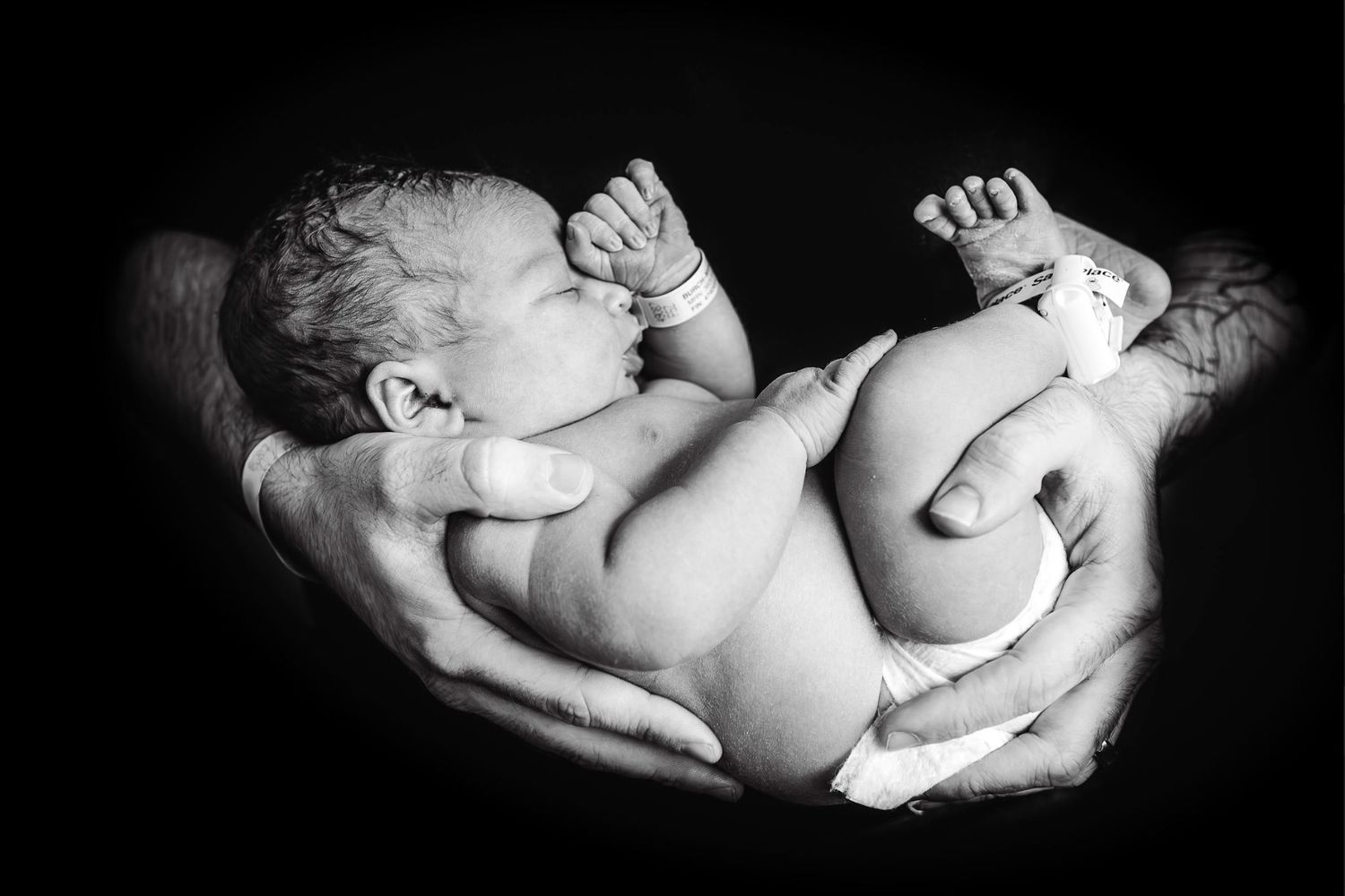 Black and white portrait of a newborn baby being gently cradled in adult hands.