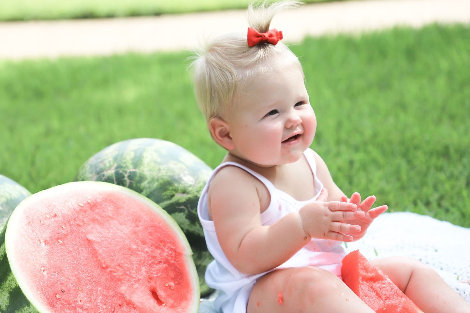 Smiling baby girl sitting beside watermelons during a summer portrait session