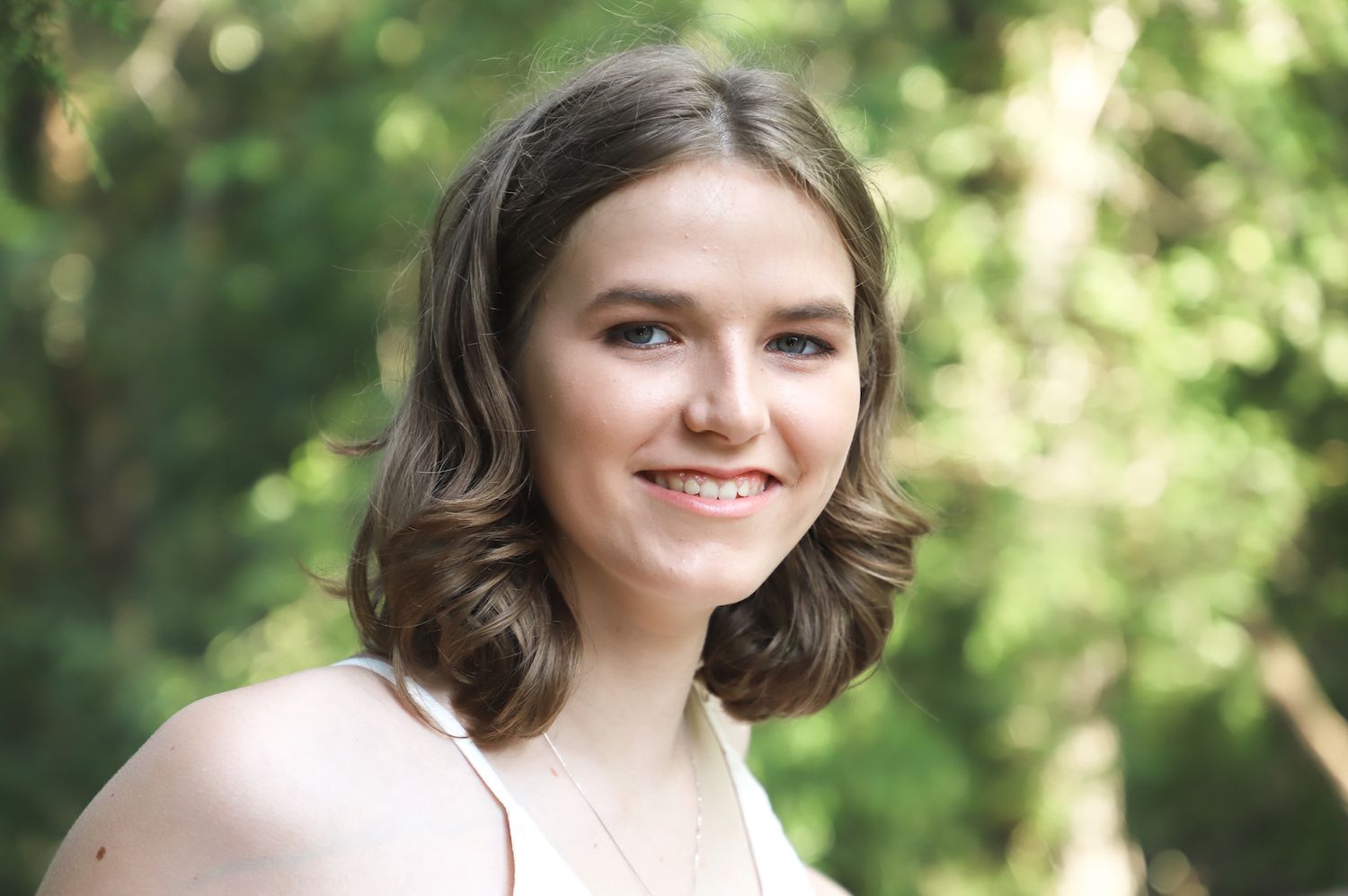 Smiling senior photographed outdoors against soft green foliage