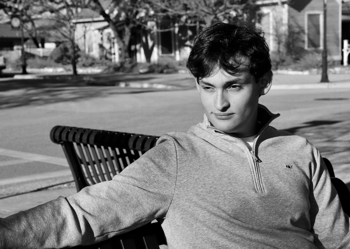 Black-and-white senior portrait of a young man seated on a downtown bench