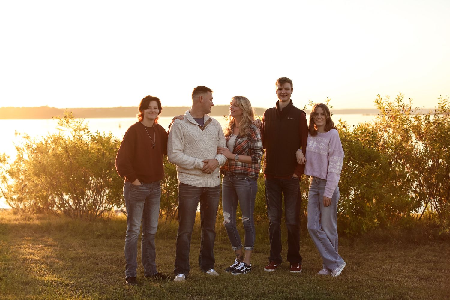 Family of five standing beside a lake at sunset