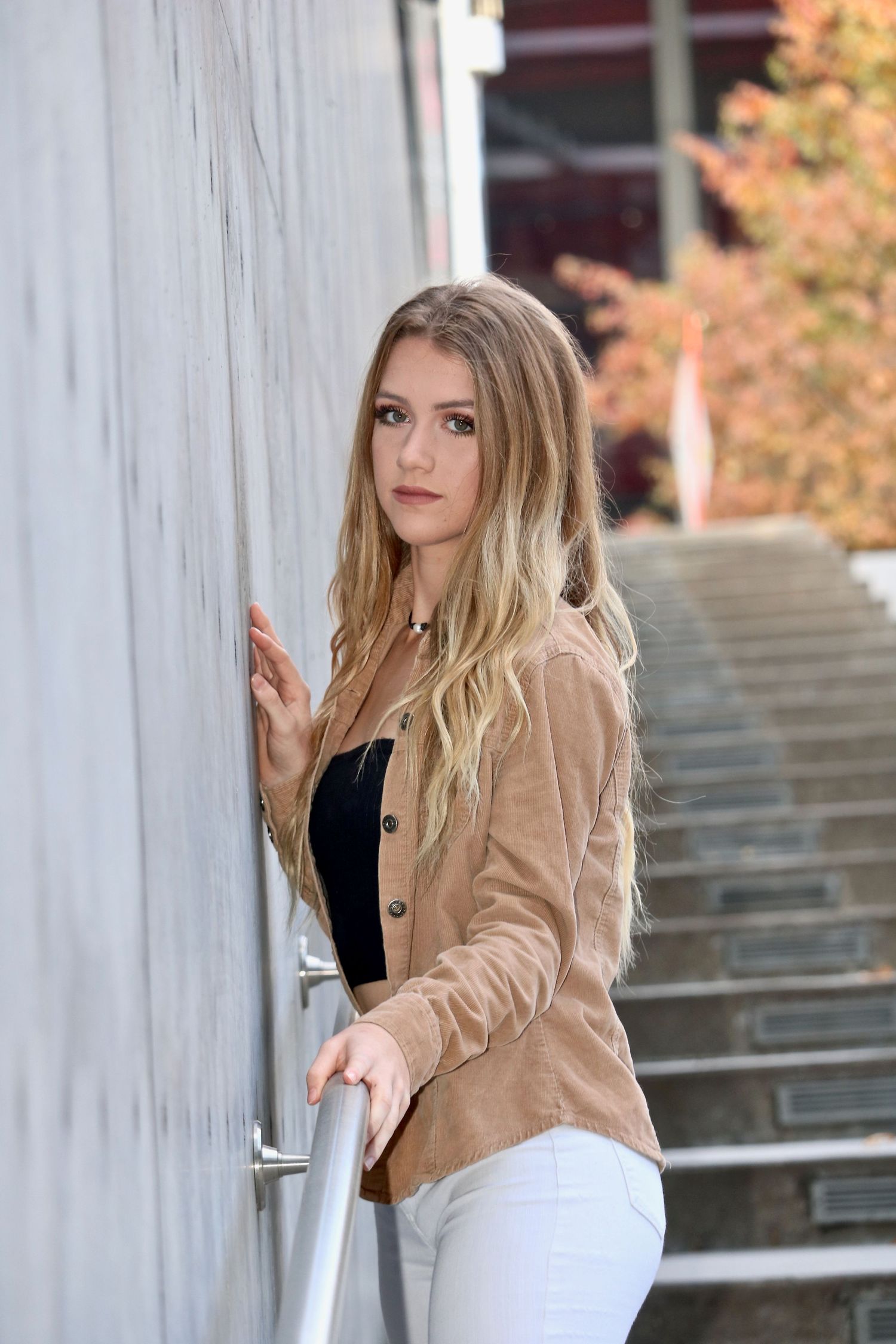 Blonde high school senior leaning against a modern wall near outdoor steps