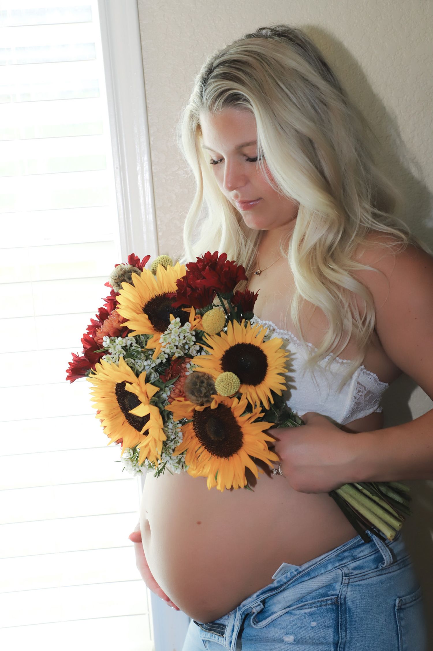 Expectant mother holding a sunflower bouquet beside a window